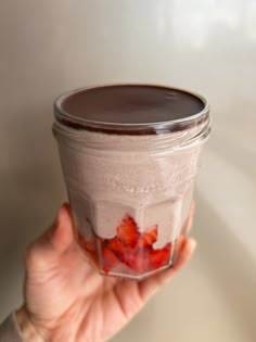 a person holding up a jar filled with chocolate and strawberries in it's hand