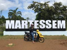 a person sitting on a motor scooter in front of a sign that says martessm