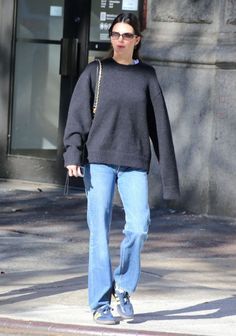 a woman in black sweater and jeans walking down the street