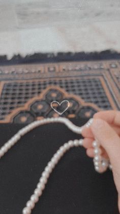 a person is holding pearls and string on a rug with a heart shaped bead in the middle