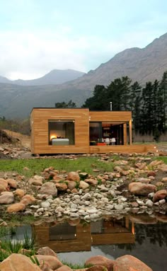 a small wooden cabin sitting on top of a lush green hillside next to a river