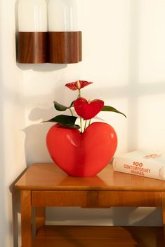 a red heart shaped vase with flowers in it on a table next to a book