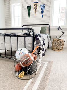 a basket filled with sports balls sitting on top of a floor next to a bed