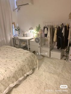 a bed room with a neatly made bed next to a desk and clothes on hangers