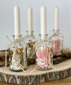 four glass jars with flowers in them sitting on a wood slab next to some candles