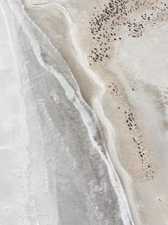 an aerial view of the beach and ocean with black dots in the sand on it