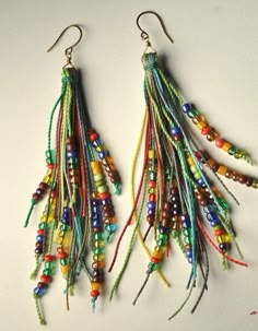 two pairs of multicolored beaded earrings hanging from hooks on a white surface