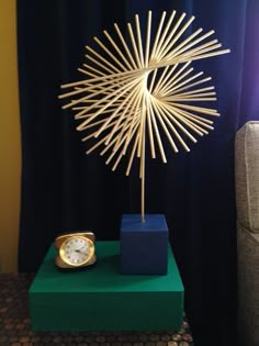 a clock sitting on top of a green box next to a sunburst sculpture