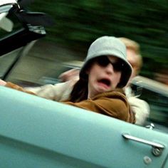 a woman driving in the back seat of a blue car with a surprised look on her face