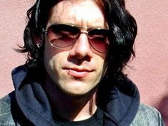 a man with long black hair wearing sunglasses and a hoodie looking at the camera