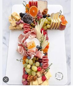 a cross made out of fruits and cheeses on a white cutting board with the letter t