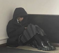 a person sitting on the floor with their legs crossed and wearing black boots, hoodie and striped skirt