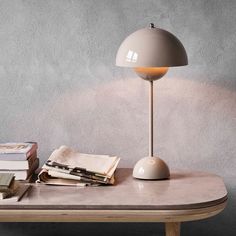 a table with a lamp and books on it next to a gray wall in the background