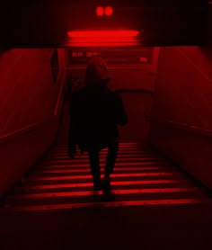 a person walking up some stairs with red light coming from the ceiling and on their back