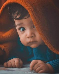 a baby is laying under a blanket and looking at the camera with an intense look on his face