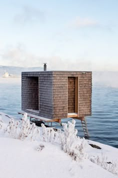 a small wooden structure sitting on top of a snow covered hill next to the ocean