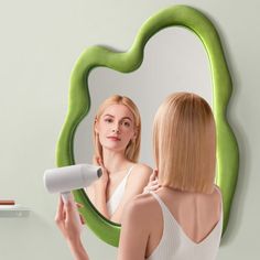 a woman blow drying her hair in front of a mirror with an oval shaped frame