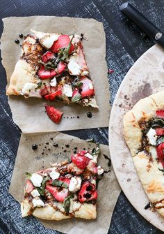 two slices of pizza with strawberries and feta cheese on top, sitting on parchment paper