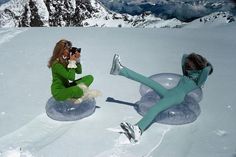 two women are sitting on inflatable snow tubs and taking pictures with their cell phones