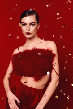 a woman with dark makeup and red feathers on her chest, standing in front of confetti