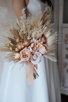 a woman in a white dress holding a bouquet of dried flowers and grasses on her wedding day