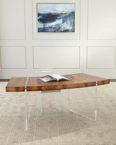 a wooden table with acrylic legs and a book on it in front of a white wall