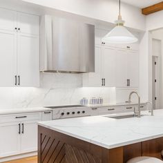 a kitchen with white cabinets and marble counter tops, along with an island in the middle