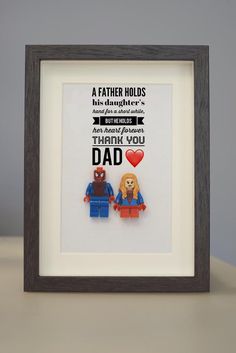 a father holds his daughter's hand as they stand in front of a lego frame