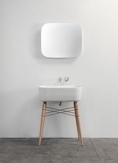 a white sink sitting under a mirror next to a wooden stand with a faucet