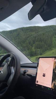 the dashboard of a car with an electronic device in it's center console and mountains in the background