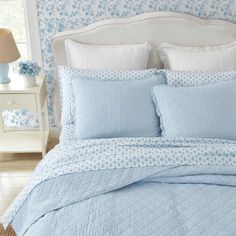 a bed with blue and white comforters in a bedroom next to a night stand