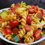 a pasta salad with tomatoes, cucumbers and zucchini in a white bowl