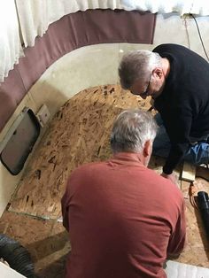 two men are working on the floor in a room with wooden boards and plywood