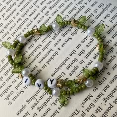 a green bracelet with white beads and leaves on top of an open book, next to the word love