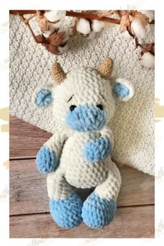 a crocheted blue and white cow sitting on top of a wooden floor next to cotton