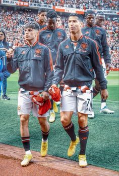 two soccer players are walking on the field with their team mates in front of an audience