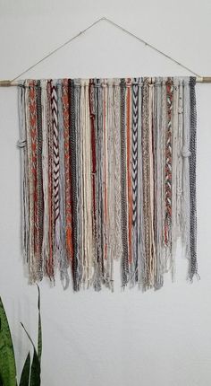 a wall hanging made out of different colored yarns and fringes next to a potted plant