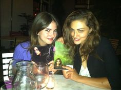 two young women sitting at a table with books and drinks in front of them, posing for the camera