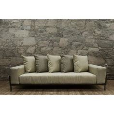 a couch sitting in front of a stone wall with four pillows on top of it