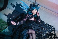 a woman with blue hair and black dress sitting on stairs talking on her cell phone