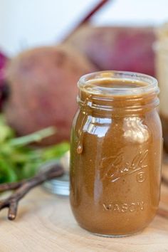 a mason jar filled with brown liquid sitting on top of a table next to vegetables