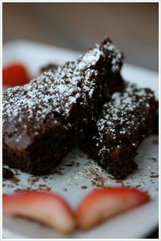 two pieces of chocolate brownie on a plate with strawberries and powdered sugar