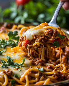 a fork full of spaghetti being lifted from a casserole dish with meat and cheese