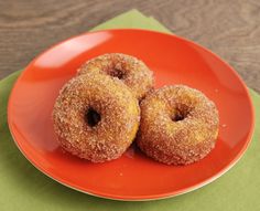 two sugared doughnuts on an orange plate next to a green place mat