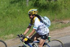 a woman riding a bike down a road with a backpack on the back of it