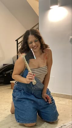 a woman sitting on the floor with her toothbrush in her mouth and wearing overalls