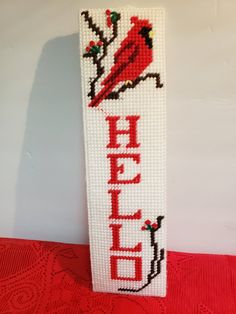 a cross stitch bookmark with the word hello written in red and a cardinal on it