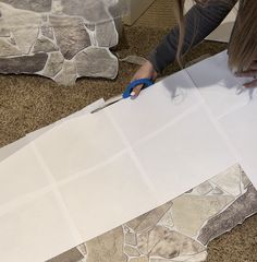 a person cutting out paper with scissors on top of the floor in front of them