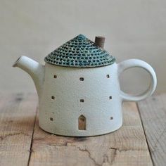 a ceramic teapot with a small house on it's top sitting on a wooden table