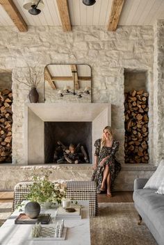 a woman sitting on a couch in front of a fire place with logs stacked behind her